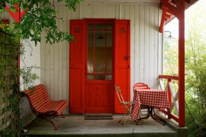 Entrée avec porte rouge et volets assortis, banc et table rouge à carreaux