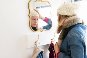 Jeune femme en train d'ajuster son bonnet dans le miroir de l'entrée